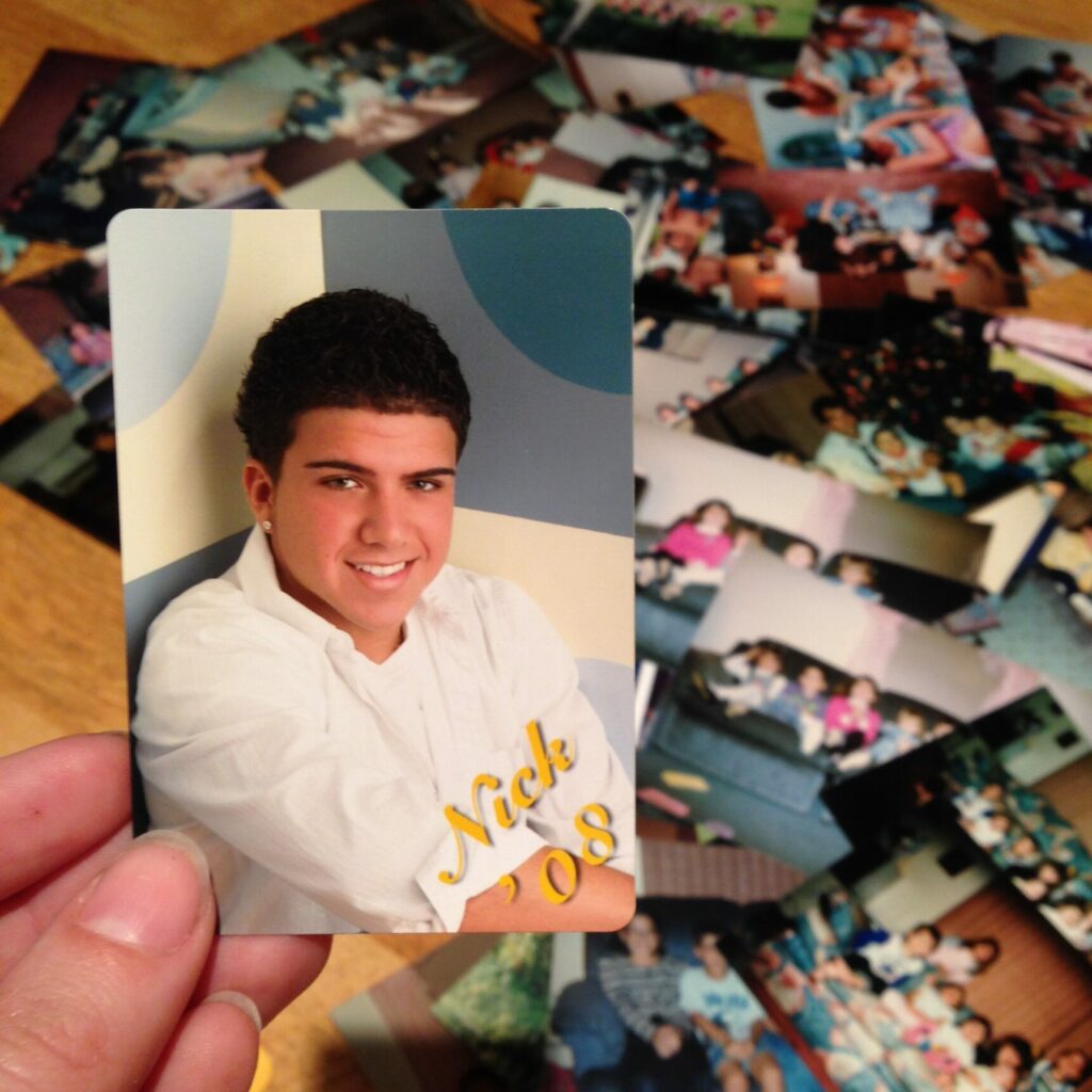 photo of Nicholas Wayne Fernandes held in a woman's hand against a background of other photos